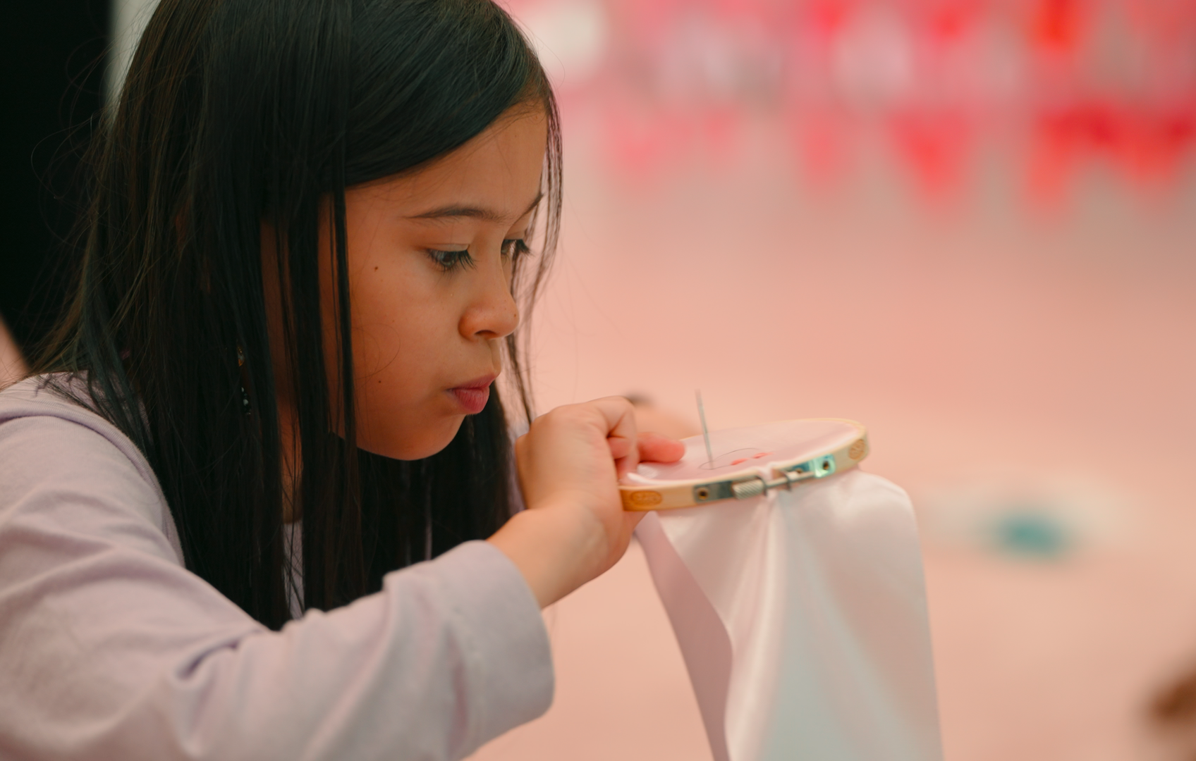 Aziatisch meisje dat borduurt met een roze zijden lint waar een borduurcirkel om heen zit