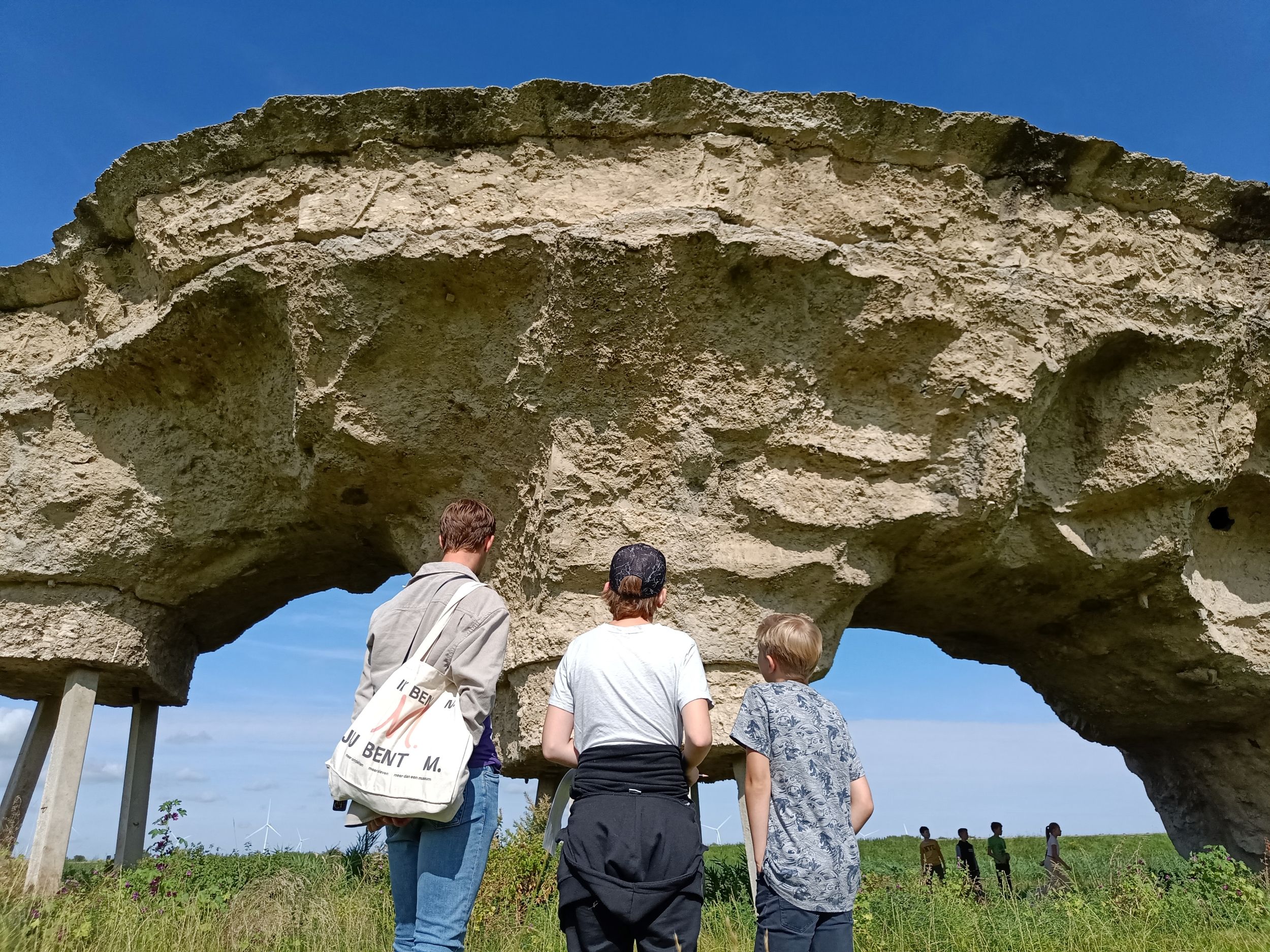 3 mensen die voor een grote rots achtig kunstwerk staan