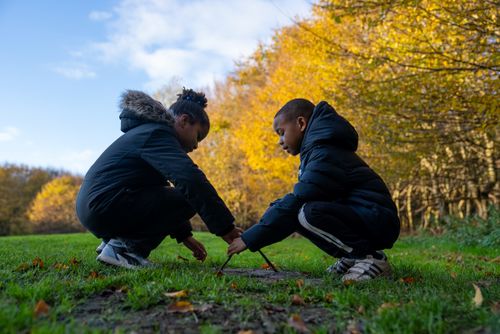 2 kinderen die met stokken in het gras spelen. gele bomen op de achtergrond