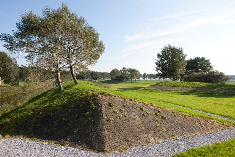 landschapskunstwerk in flevoland. stenen piramide in grasveld met bomen er boven